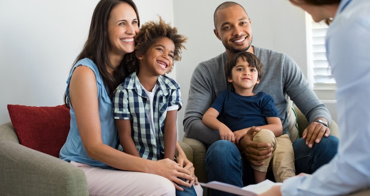 A happy, bi-racial family with two kids having a counseling session with a therapist.