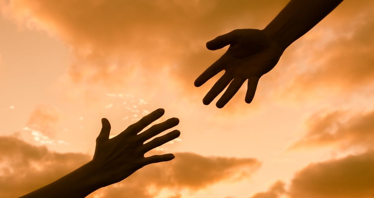 Two hands reaching out to each other in the orange sky filled with clouds.